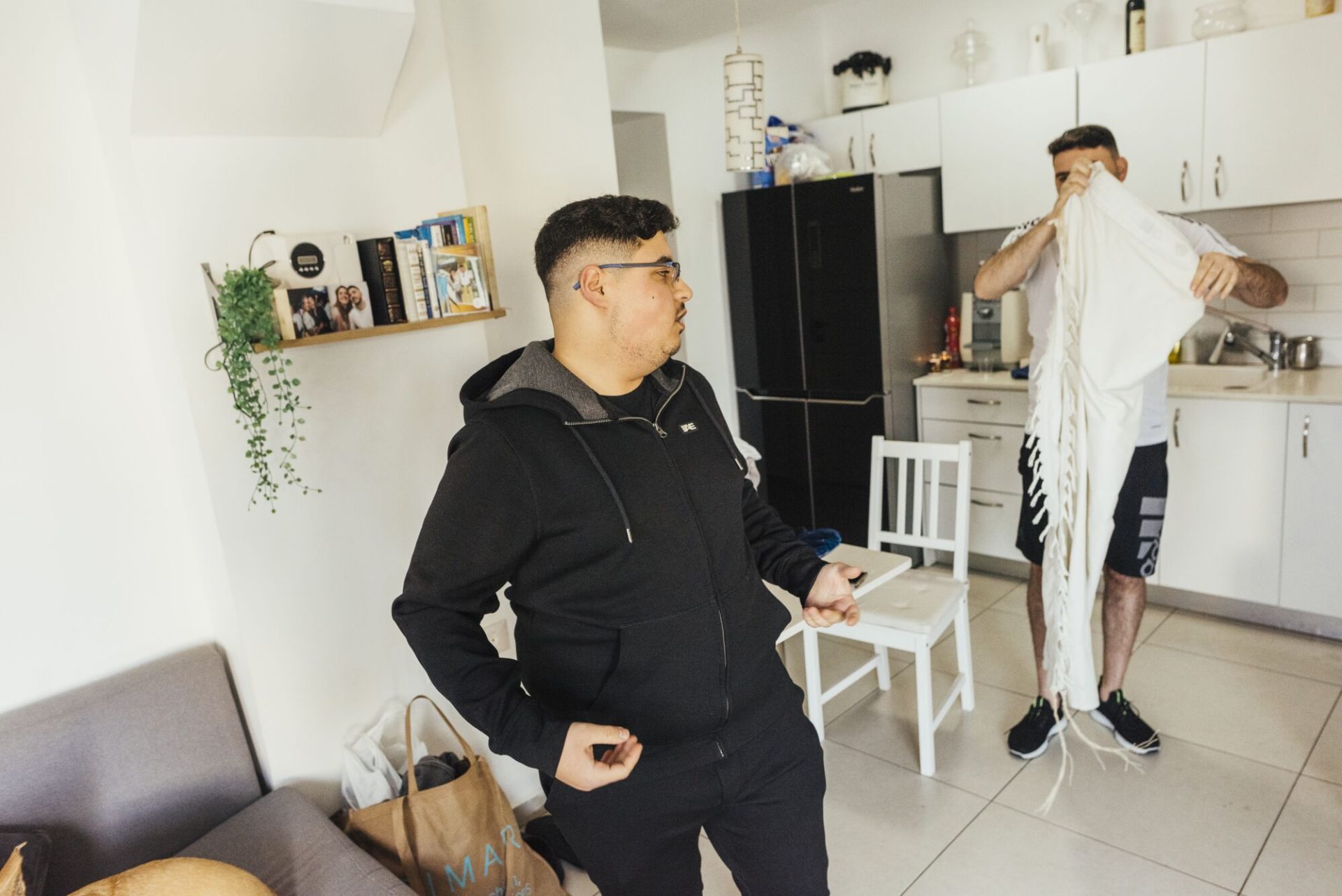 A man, left, in black clothing stands across from another man holding a shawl in an apartment 