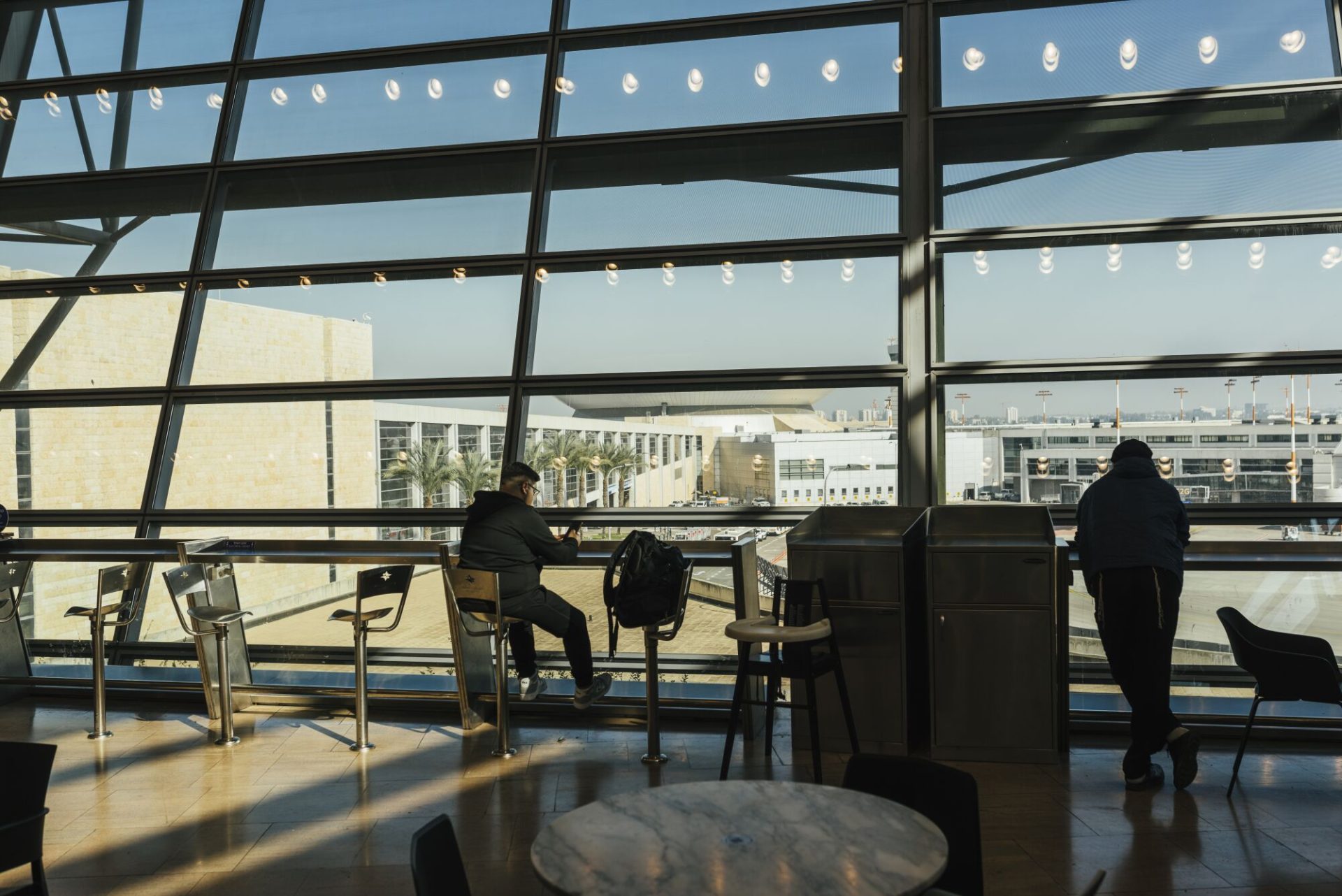 A man sits in an airport lounge with glass windows facing buildings